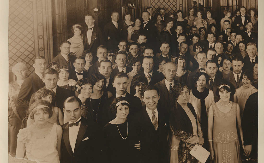 An old photo from the 1920s featuring dozens of fancily dressed people in an ornate room.