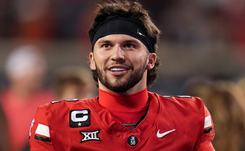 A man in a red football jersey wearing a black headband and no helmet.