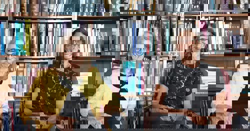 Brooklyn Law School professor Maryellen Fullerton (left) sits next to fellow professor Stacy Caplow in front of a bookshelf.