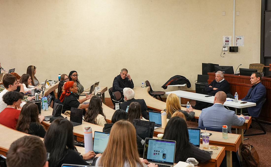 Students in a lecture hall taking notes on laptops during a discussion.