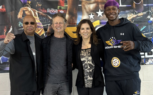 Four people pose in front of a boxing banner with two men on the left, followed by a woman and another man.