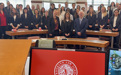 A couple dozen people pose in a classroom with a monitor depicting the Brooklyn Law School shield front and center.