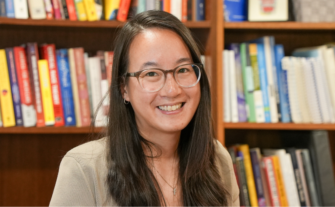A woman with long hair and glasses smiling in front of a bookcase.
