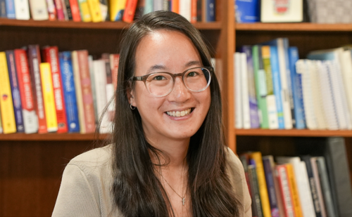 A woman with long hair and glasses smiling in front of a bookcase.