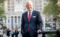 A man in a suit and tie poses in front of a courthouse in Brooklyn, New York.