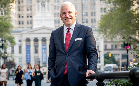 A man in a suit and tie poses in front of a courthouse in Brooklyn, New York.
