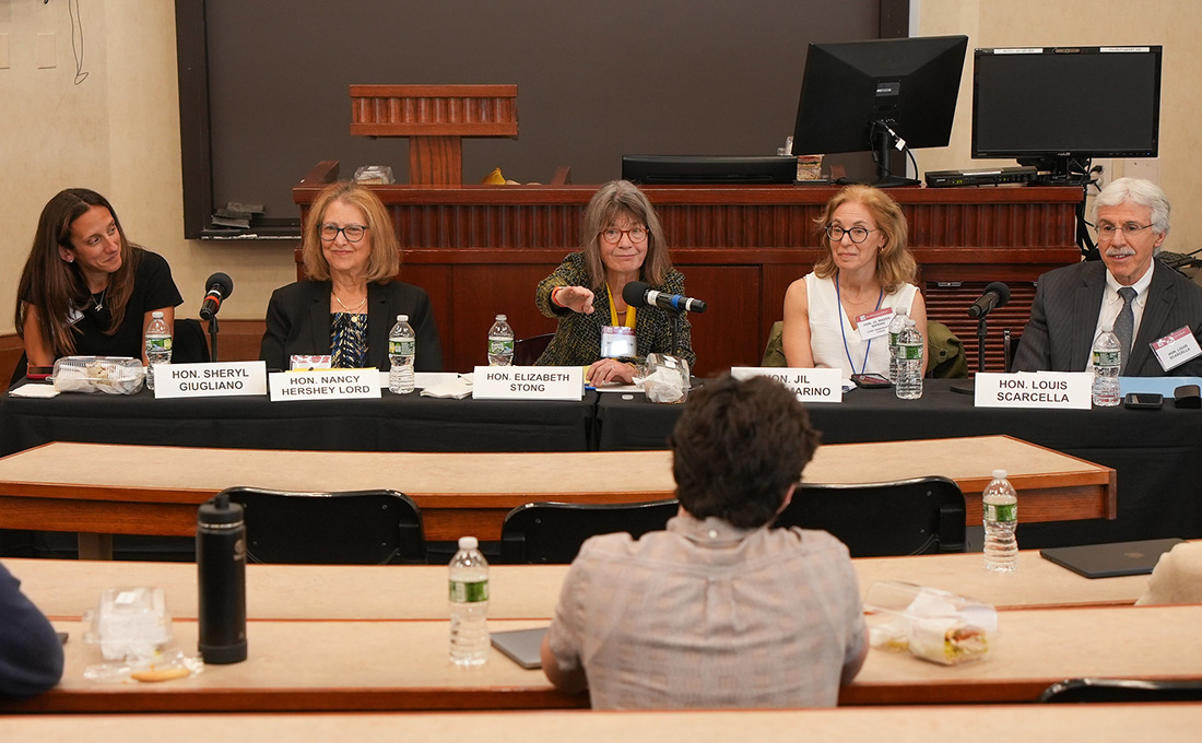 A five-person panel sits at a table and takes questions from students in a classroom.