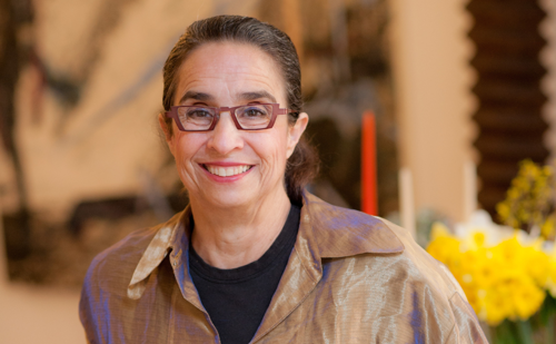 A woman with dark hair and glasses smiling.