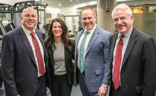 Four people, three men and one woman, pose for a picture in the new fitness center inside Feil Hall at Brooklyn Law School.