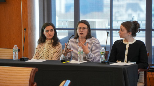 Three women seated at a table with microphones and notepads in front of them.