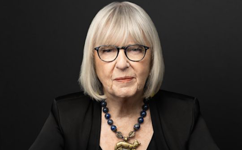 A woman in a black suit poses in front of a black background.